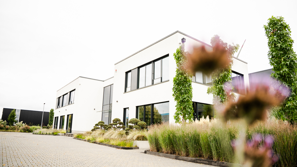 Moderne Architektur mit weißen Wänden, großen Fenstern und gepflegtem Garten.