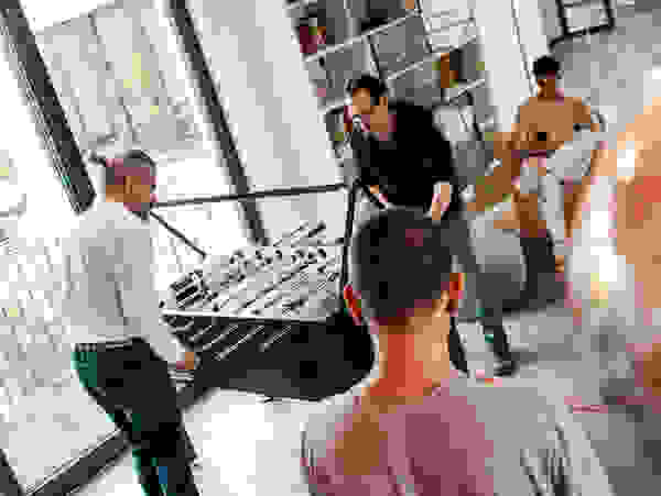 Mitarbeiter spielen Tischfußball in einer modernen, hellen Büro-Lounge, während ein weiterer Kollege auf einem Sessel sitzt und sein Handy nutzt.