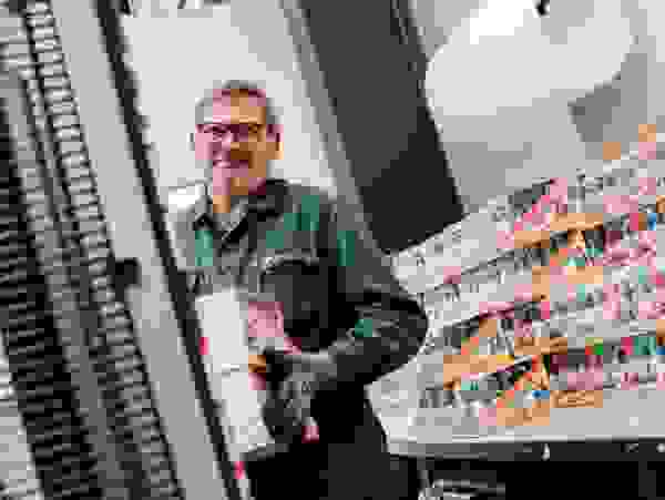 Mann mit Arbeitshandschuhen und einer Brille lächelt, während er Kartons mit Spielzeug verräumt