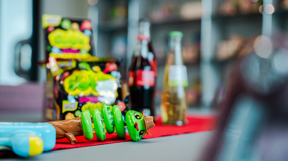 A colourful toy snake lies on a red cloth, with snacks and bottles in the background.