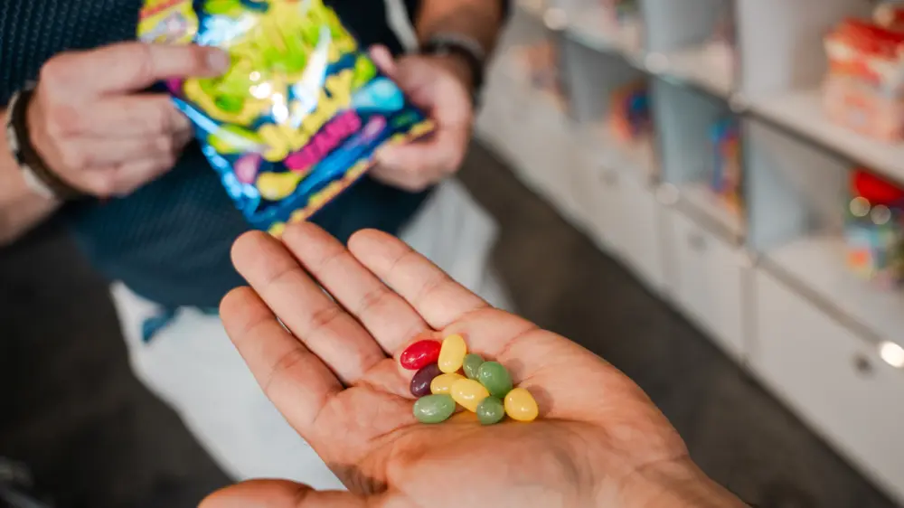 Colourful sweets lie in one hand, while another hand holds a bag of similar sweets.