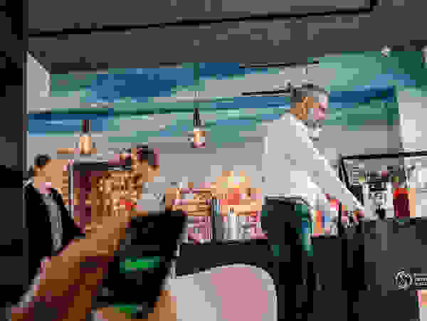 An employee playing table football in a modern office with cityscape decor, while other colleagues are talking and another person is typing on a smartphone.