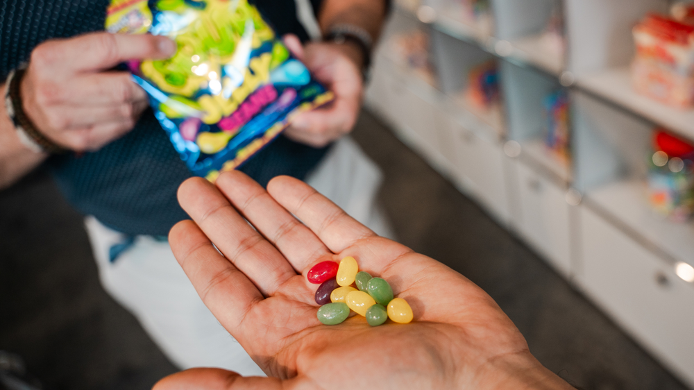 En una mano hay caramelos de colores, mientras que la otra sostiene una bolsa con dulces similares.