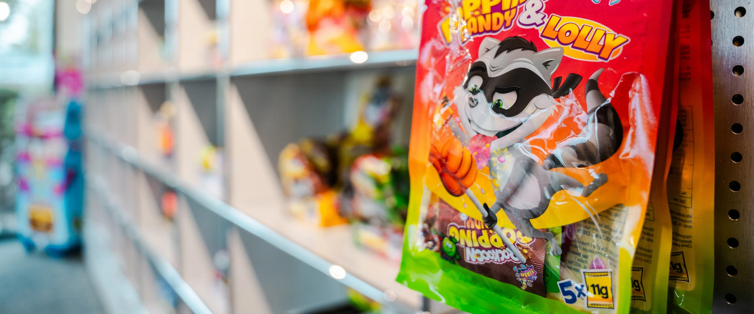 Una bolsa de caramelos con la mascota de un mapache de dibujos animados cuelga de una estantería con otros caramelos al fondo.