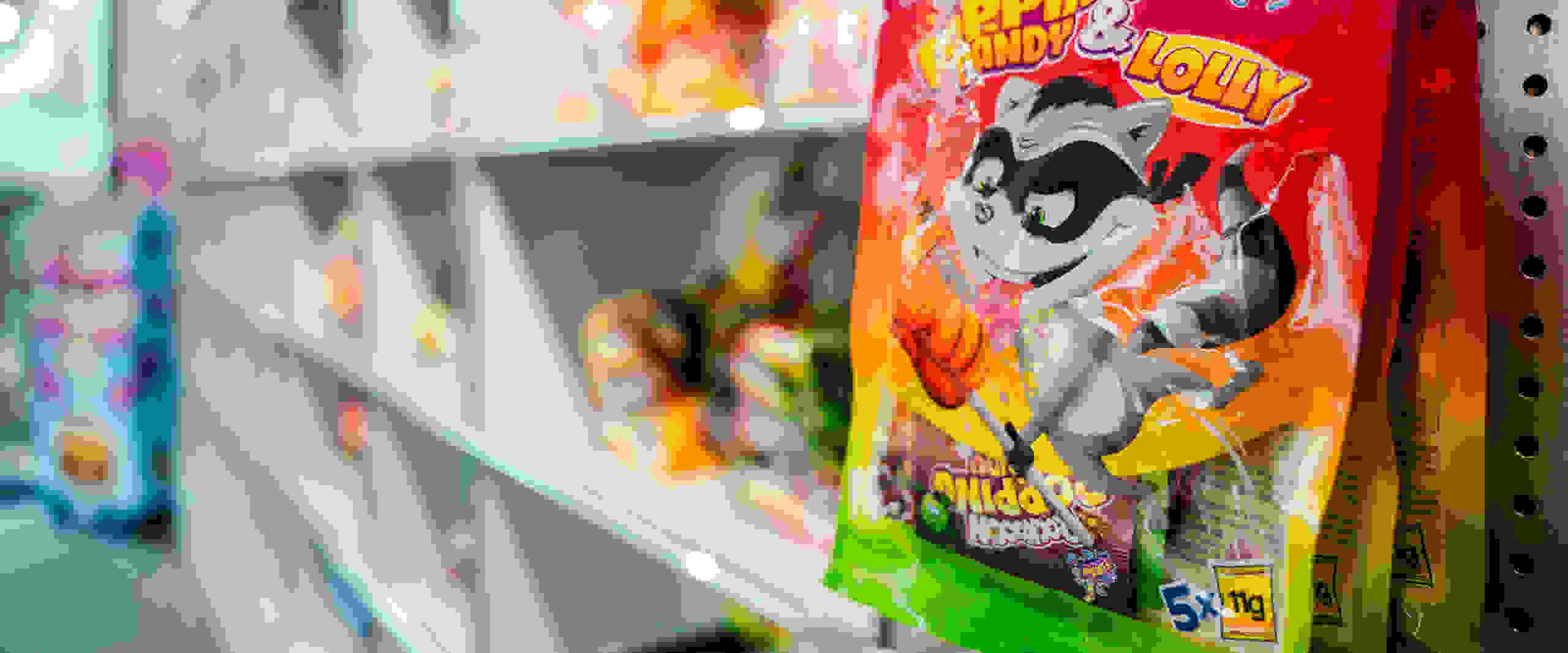 Una bolsa de caramelos con la mascota de un mapache de dibujos animados cuelga de una estantería con otros caramelos al fondo.