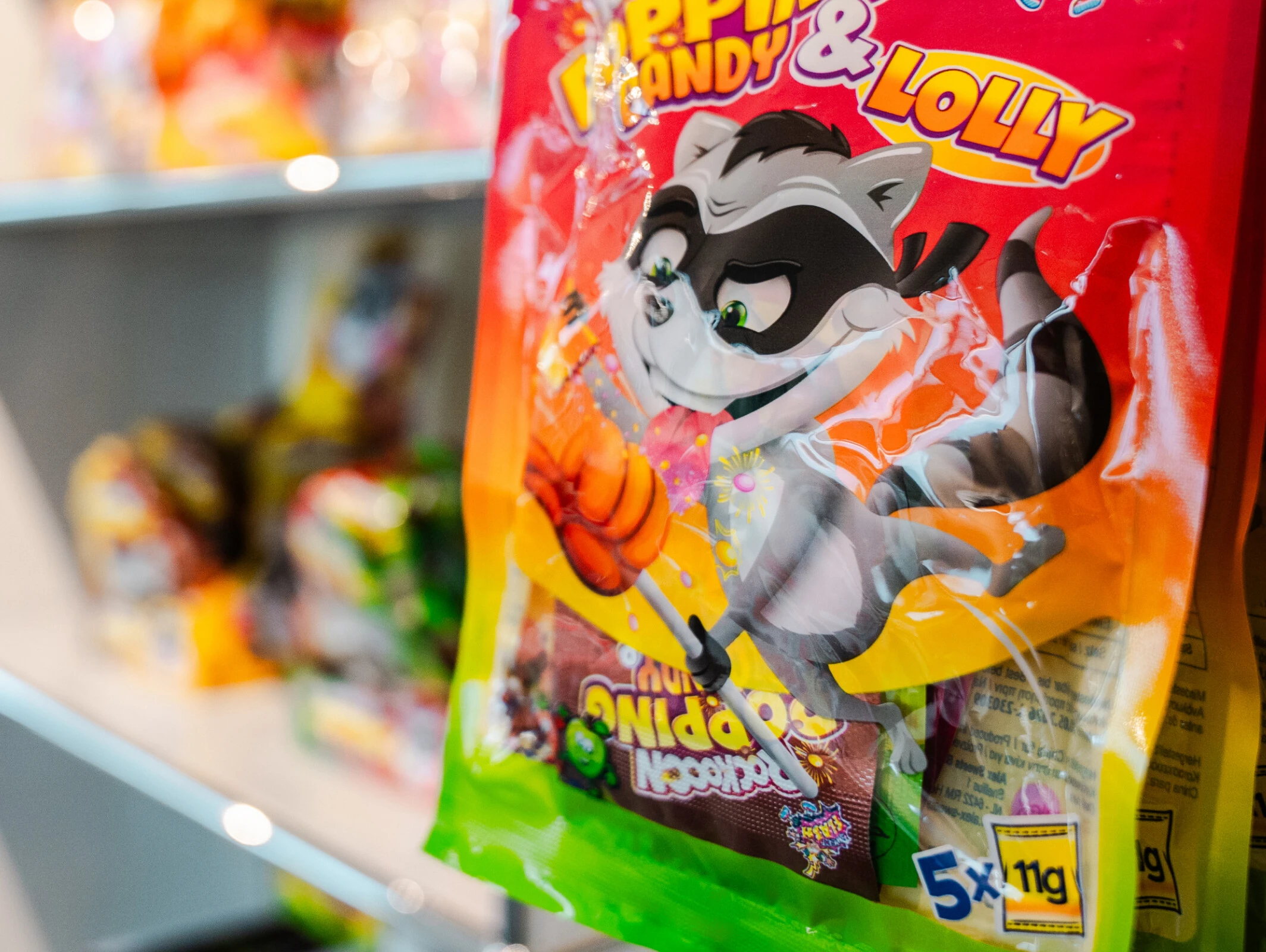 Una bolsa de caramelos con la mascota de un mapache de dibujos animados cuelga de una estantería con otros caramelos al fondo.