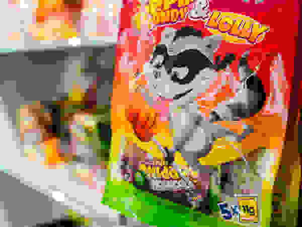 Una bolsa de caramelos con la mascota de un mapache de dibujos animados cuelga de una estantería con otros caramelos al fondo.