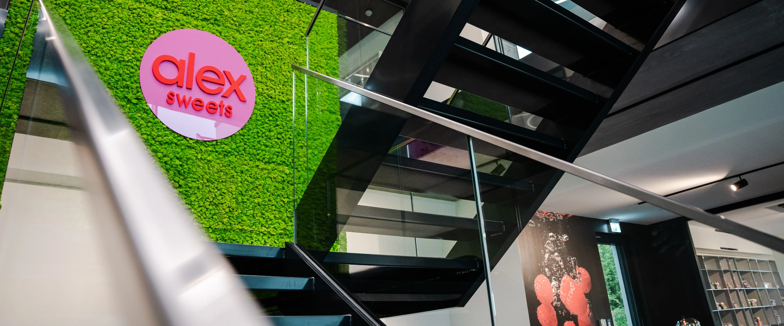 Escalier moderne avec une rampe en verre et un mur de mousse vert clair. Le logo 